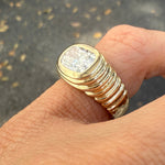 A hand wearing a 14K yellow gold pinky ring with a striped texture and a large center lab diamond.