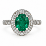 An oval emerald ring with a halo of small white diamonds, set on a silver-colored band with pavé diamonds, shown on a white background.