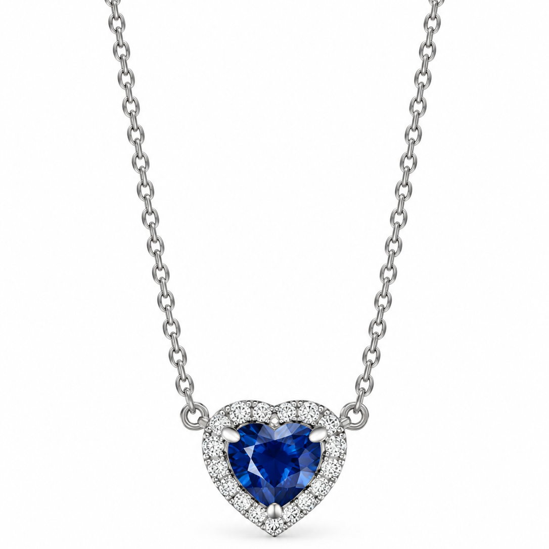 A heart-shaped pendant necklace featuring a deep blue heart-shaped sapphire surrounded by a halo of small diamonds, suspended on a white gold chain against a plain white background.