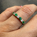 Emerald and diamond band ring in 14K yellow gold on a finger. 
