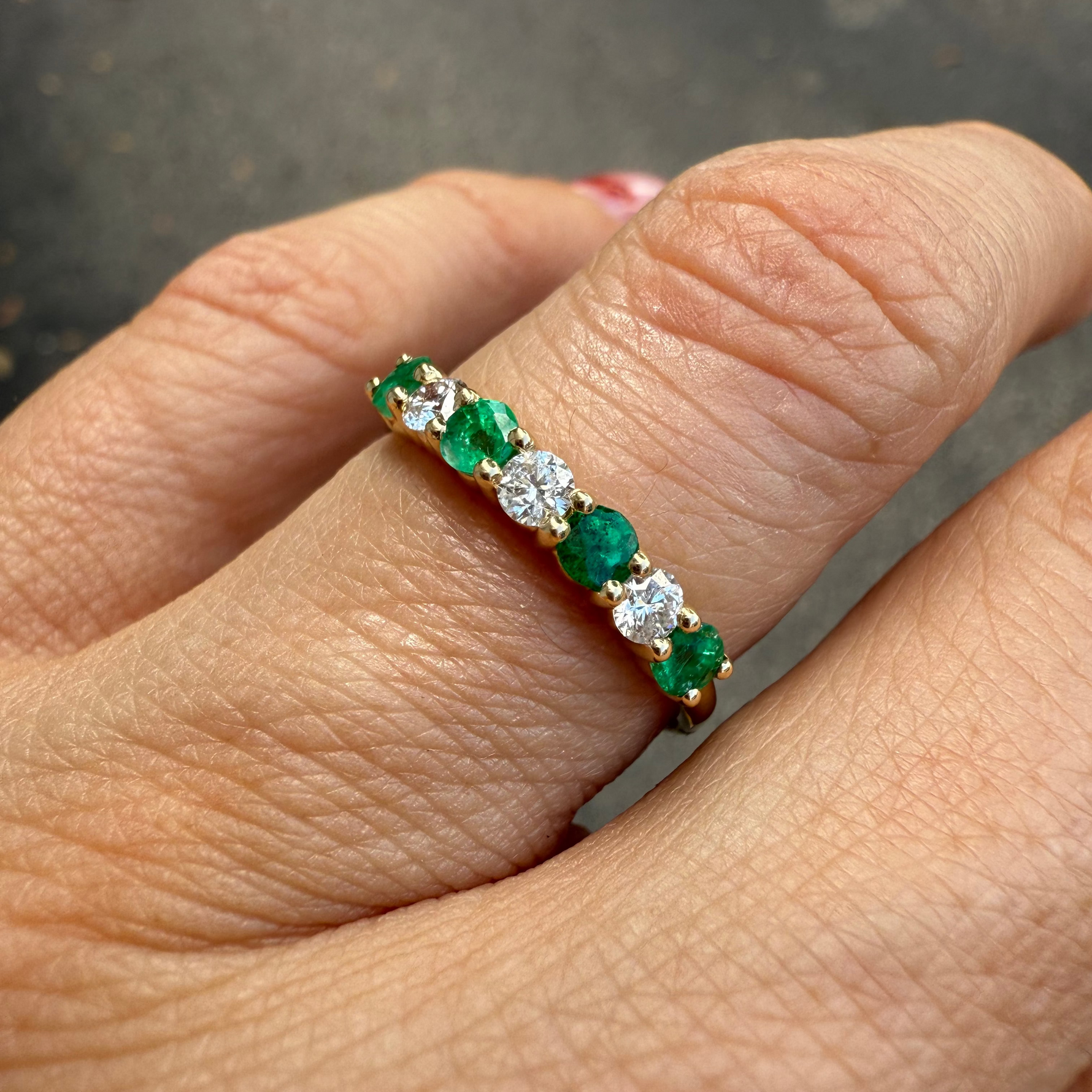 Emerald and diamond band ring in 14K yellow gold on a finger. 