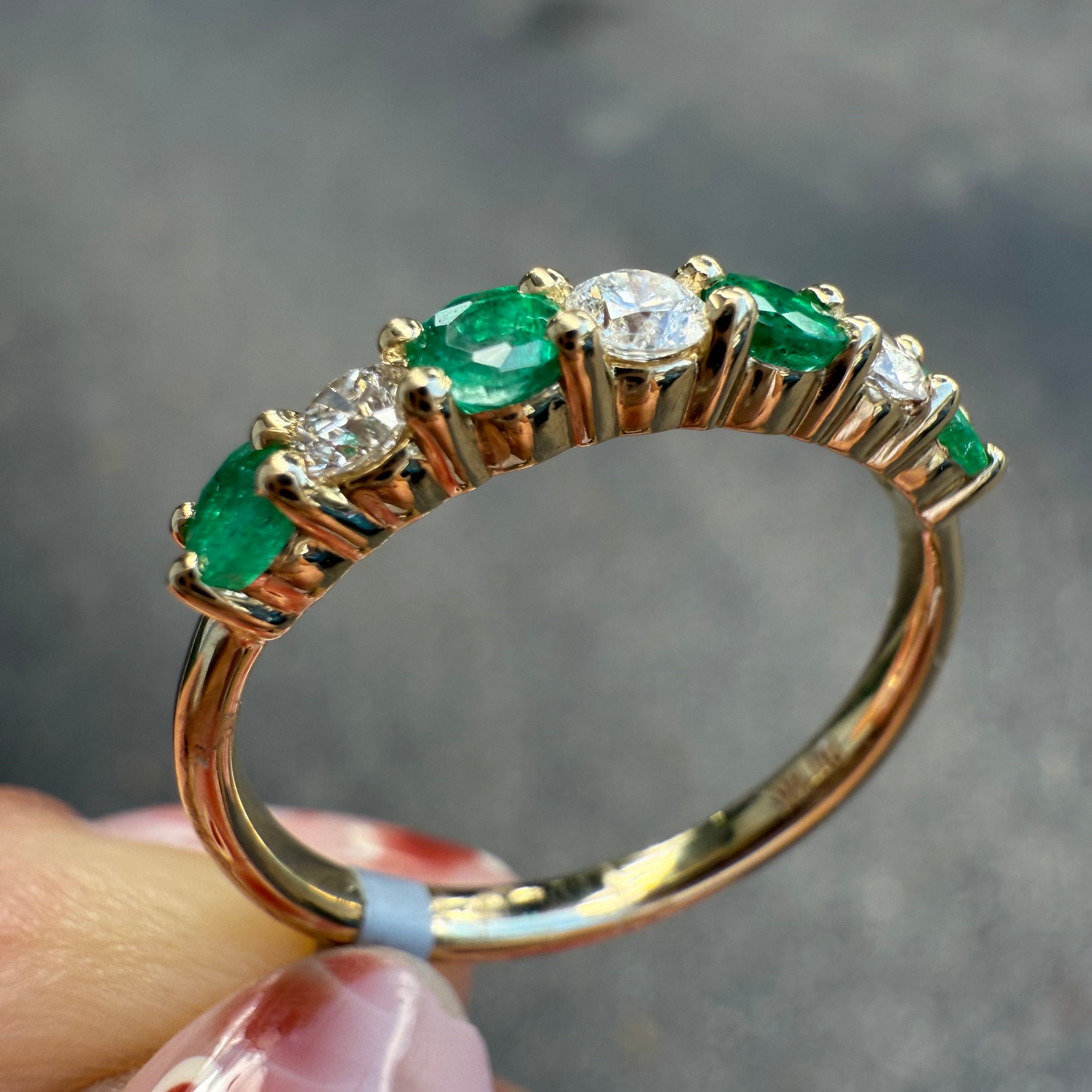 Emerald and diamond band ring in 14K yellow gold held by a hand.