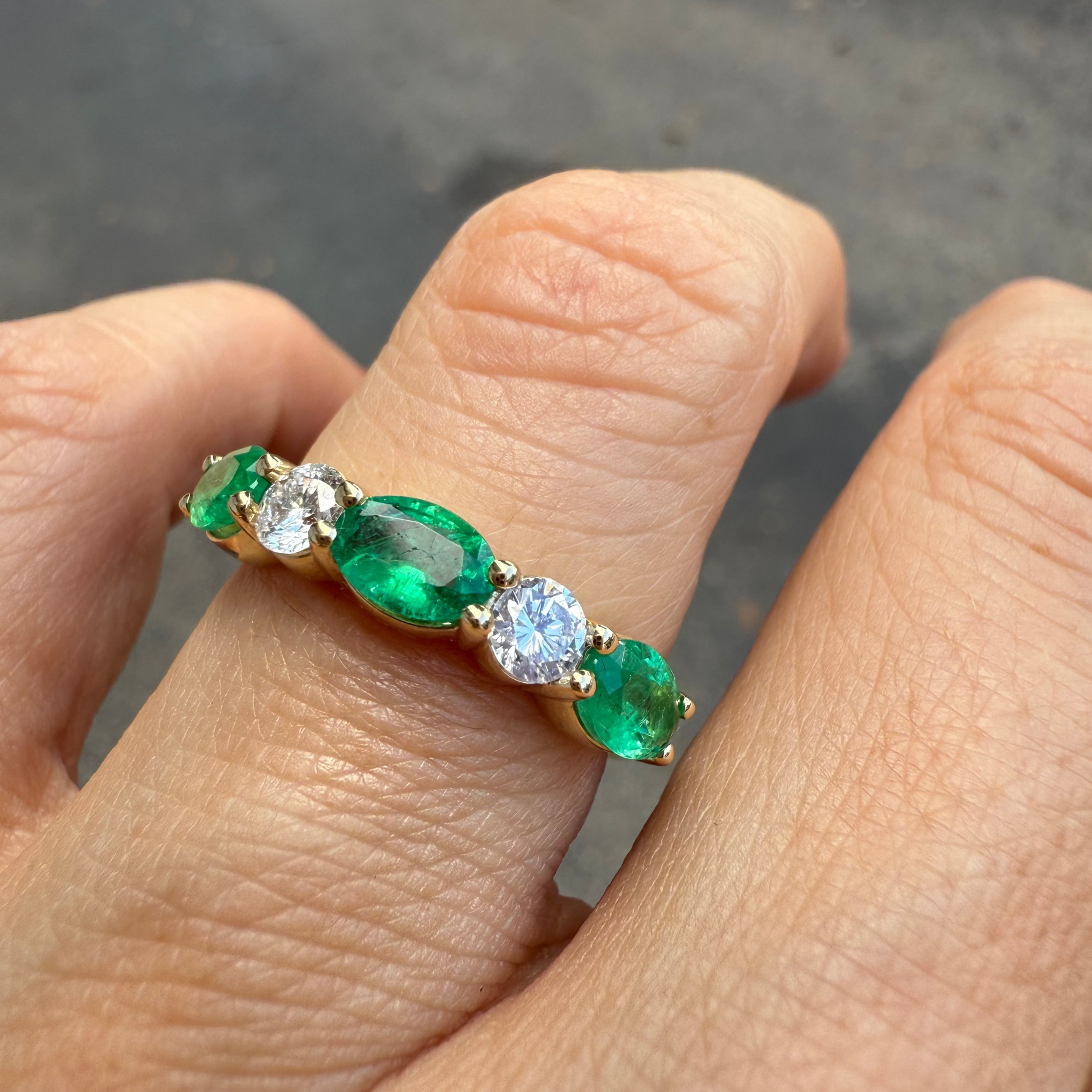 Emerald and diamond five-stone ring in 14K yellow gold on a finger.