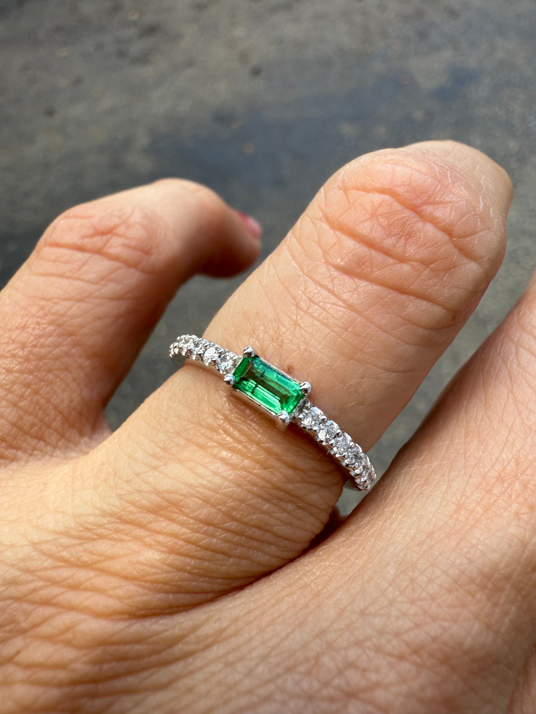 Dainty emerald and diamond ring in 14K shown on a finger