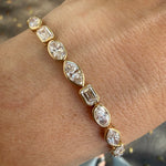 Yellow gold bezel set multi shape lab created diamond tennis bracelet on wrist. 