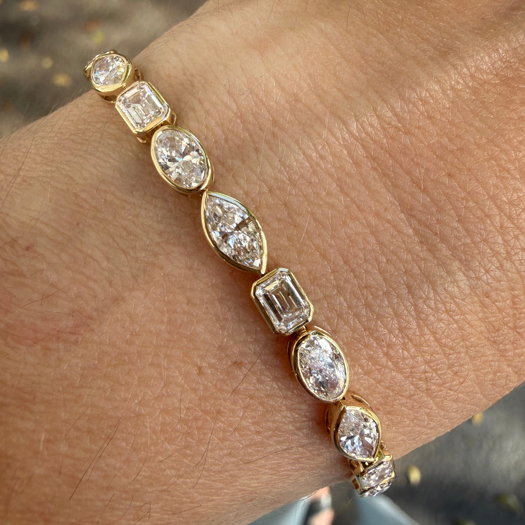 Yellow gold bezel set multi shape lab created diamond tennis bracelet on wrist. 