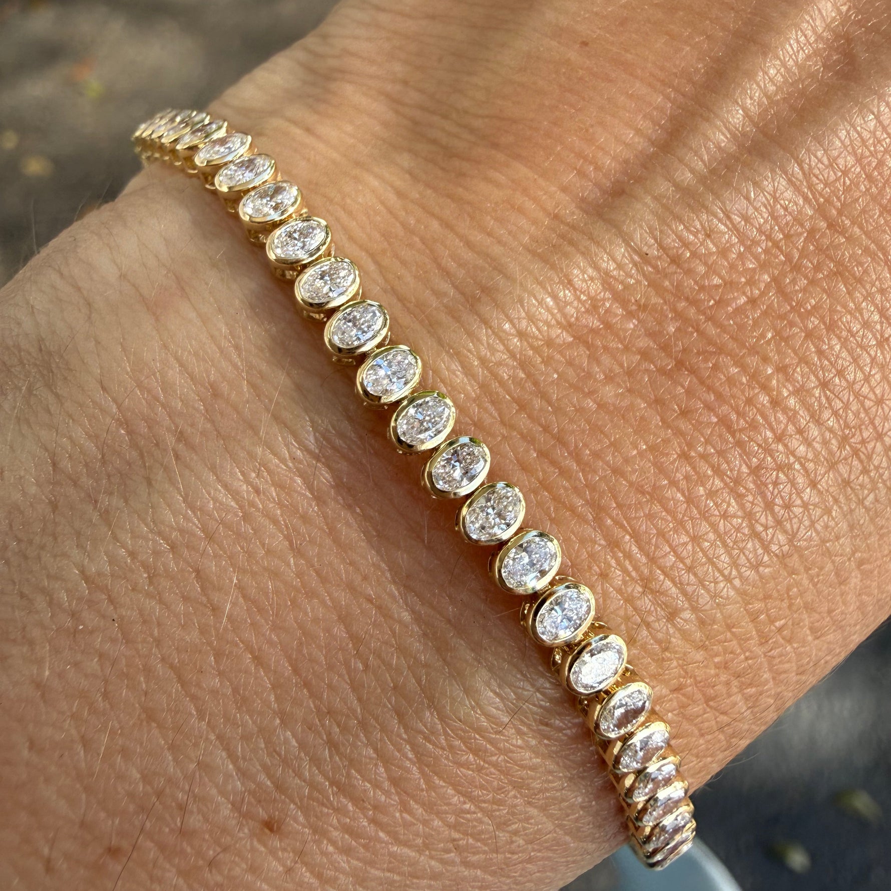 Yellow gold bezel set tennis bracelet with lab created oval diamonds. 