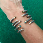 A collection of sterling silver and 14K twist bangles with various stones and pearls displayed on a person's wrist.