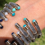 A collection of sterling silver and 14K twist bangles with various stones and pearls displayed on a person's wrist.