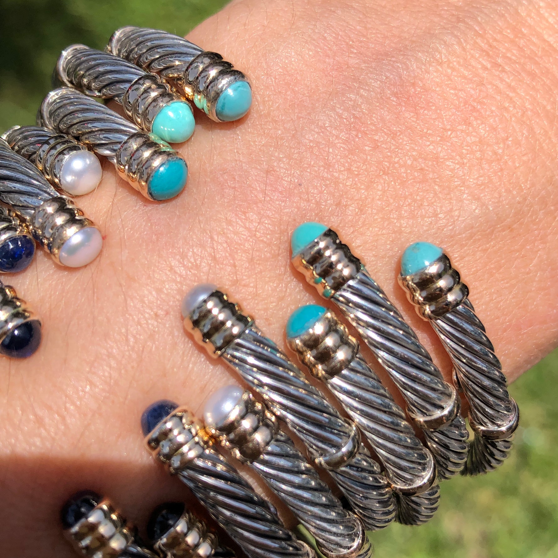 A collection of sterling silver and 14K twist bangles with various stones and pearls displayed on a person's wrist.