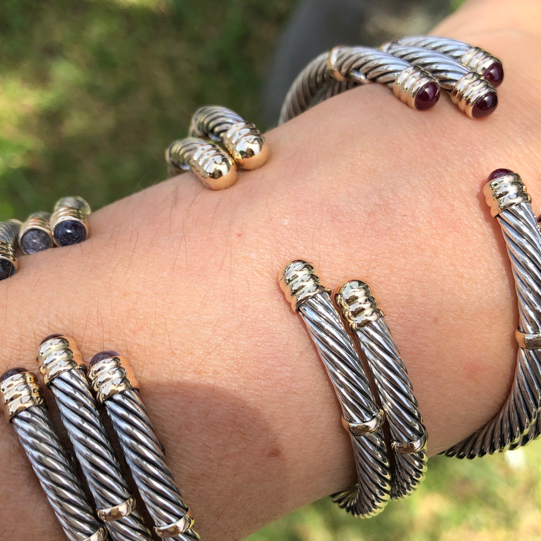 A collection of sterling silver and 14K twist bangles with various stones and pearls displayed on a person's wrist.