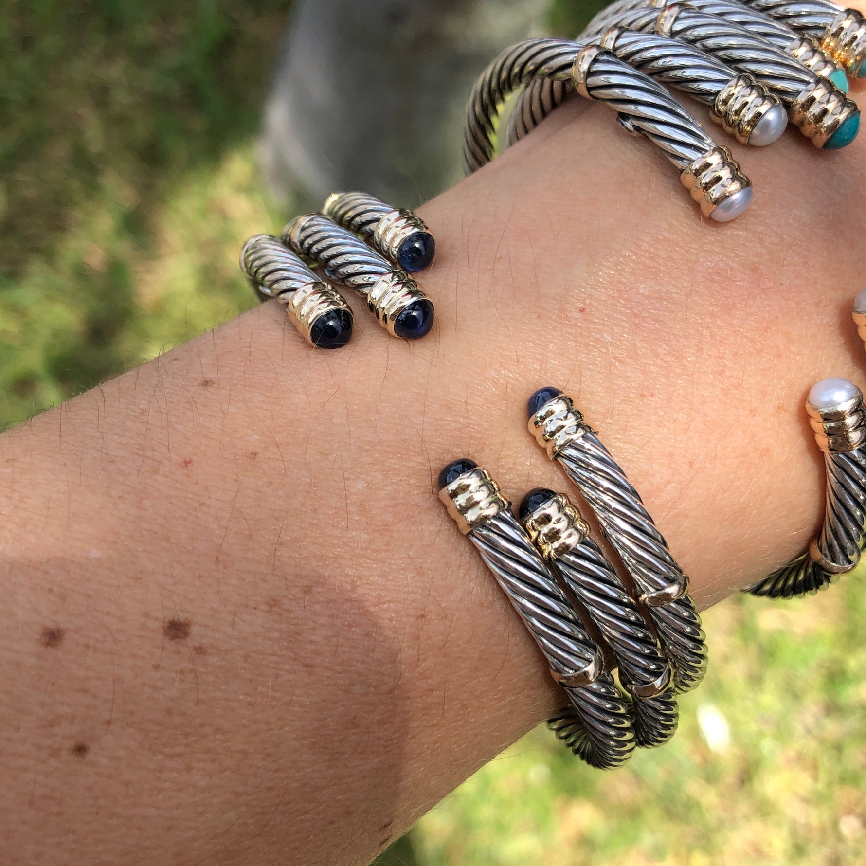 A collection of sterling silver and 14K twist bangles with various stones and pearls displayed on a person's wrist.
