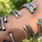 A collection of sterling silver and 14K twist bangles with various stones and pearls displayed on a person's wrist.