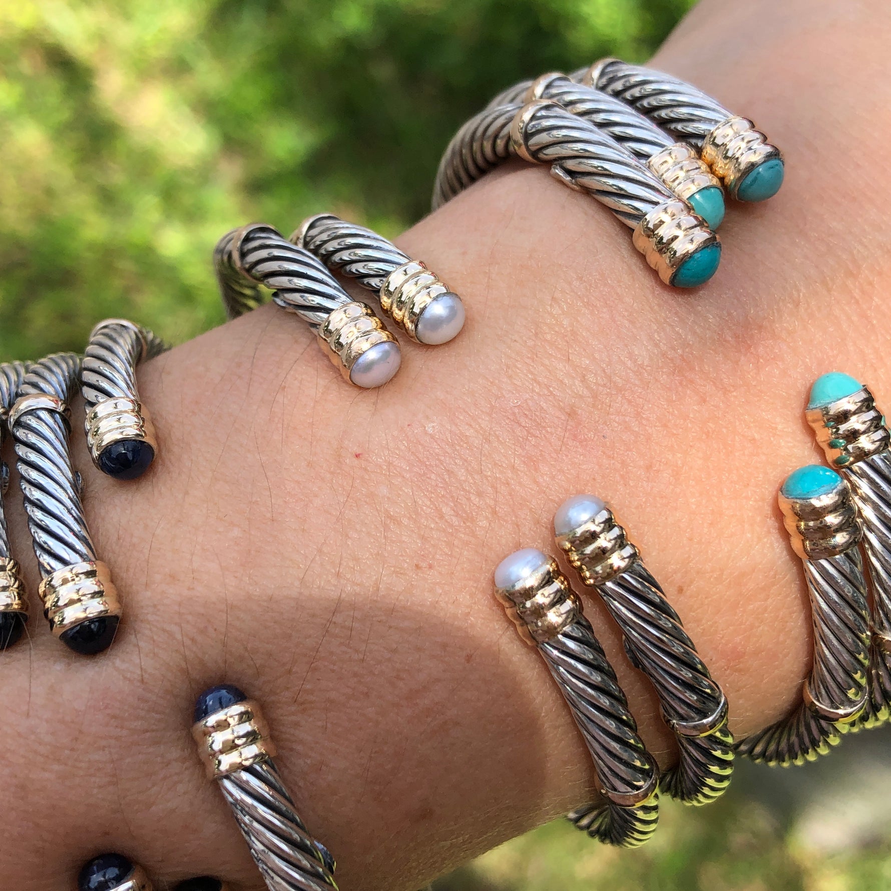 A collection of sterling silver and 14K twist bangles with various stones and pearls displayed on a person's wrist.